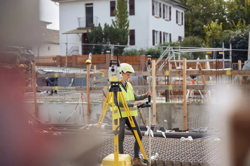 baustelle-frau-mitarbeiterin-helm-messen-detail-notieren-arbeiterin-sicherheit-haus-beton-holz-erde-tiefbau