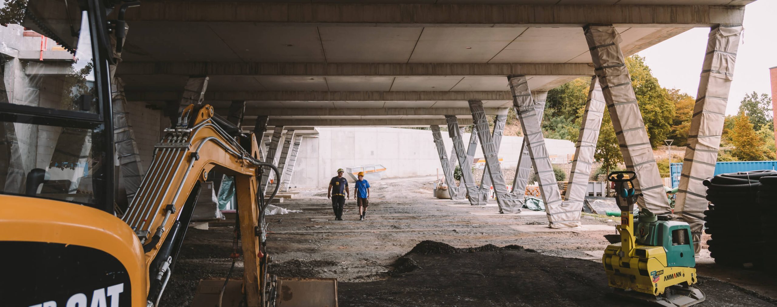 hallenbad-kriftel-bauarbeiter-mit-helm-unter-parkdeck-beton-v-stuetzen-Polier-Personen-Bagger